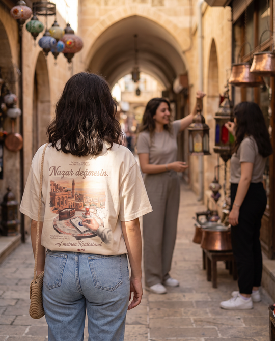 Frau im demli Nazar değmesin. Shirt in Sand von hinten in einer Basar-Gasse in Mardin