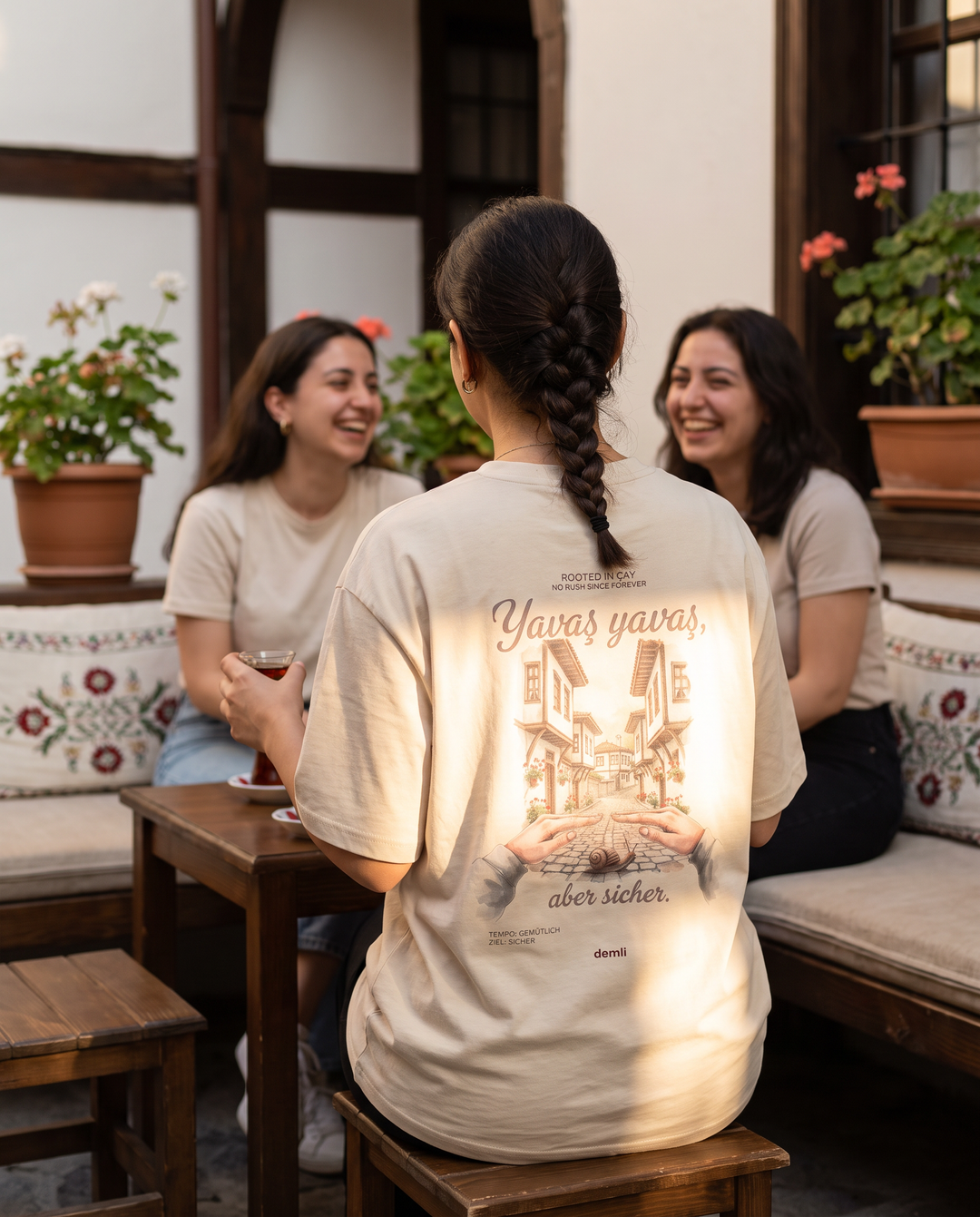 Frau im demli Yavaş yavaş Shirt in Sand von hinten in einem Innenhof-Café in Safranbolu