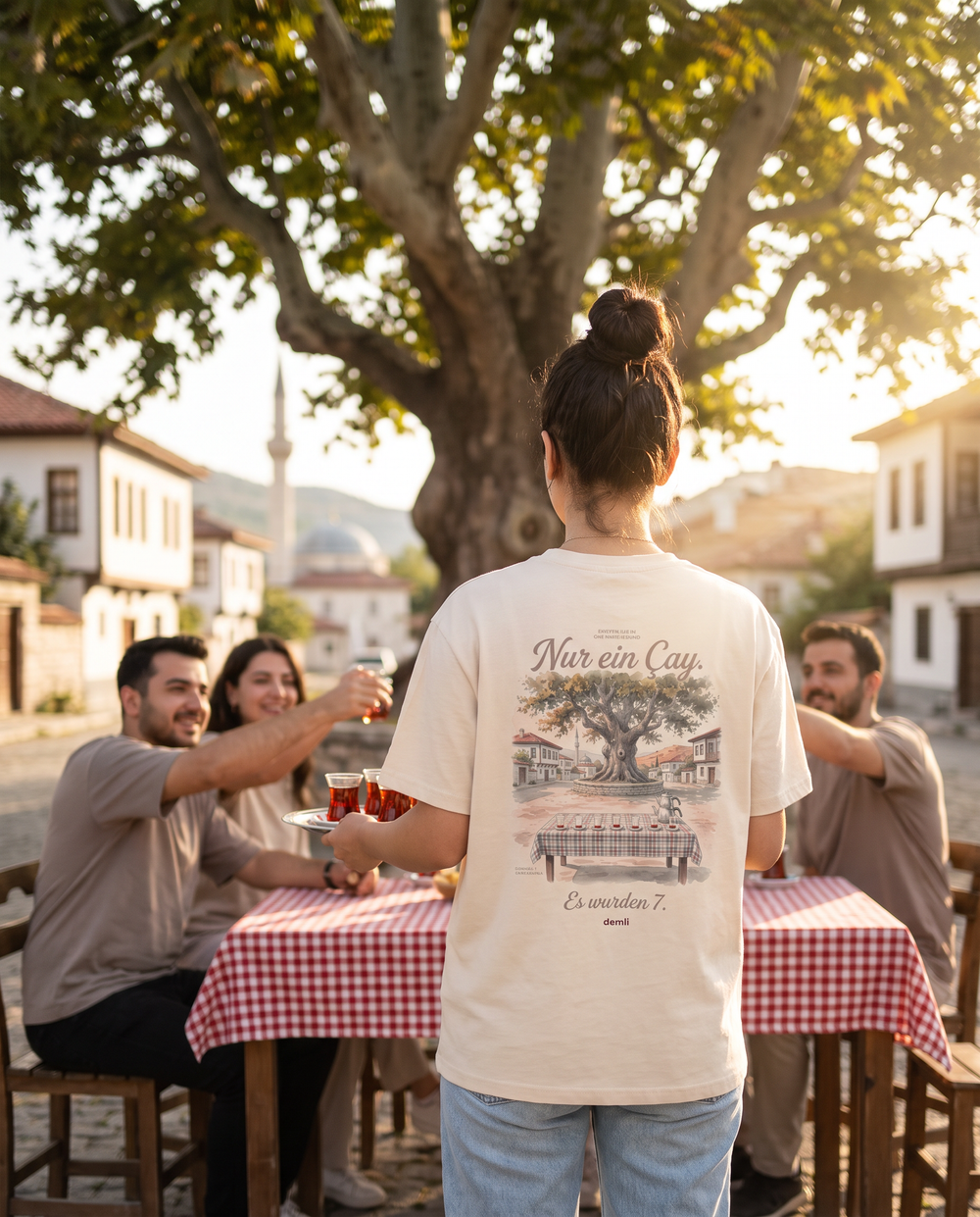 Frau im demli Nur ein Çay. Shirt in Sand von hinten serviert Tee im Dorfcafé