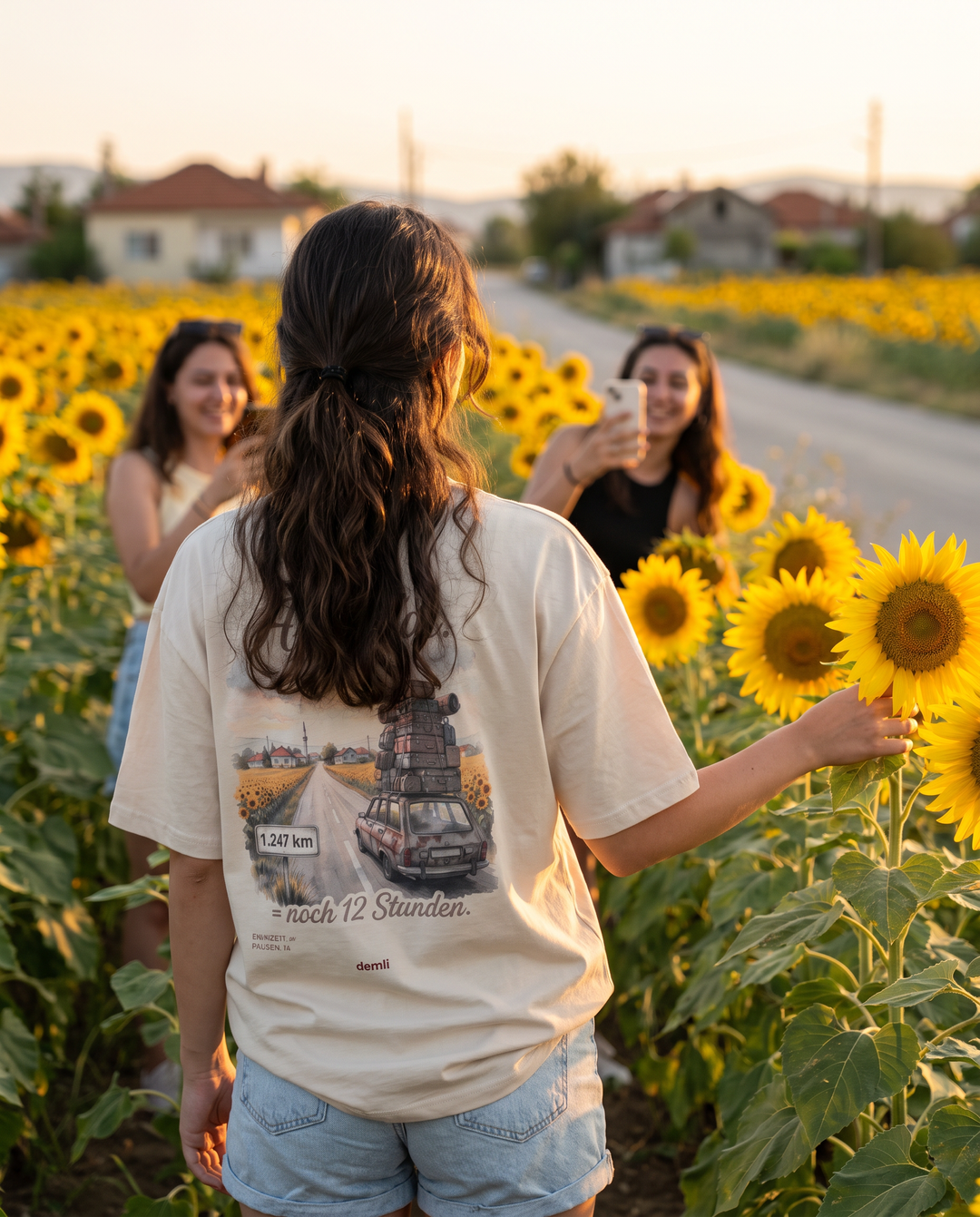 Frau im demli Az kaldı. Shirt in Sand von hinten in einem Sonnenblumenfeld bei Sonnenuntergang